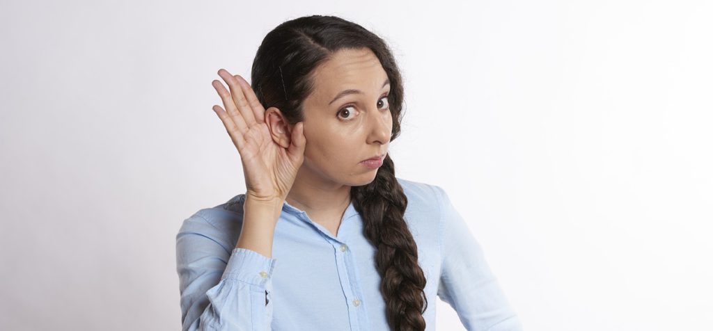 Woman in blue shirt and with long braid cups hand to ear in listening pose